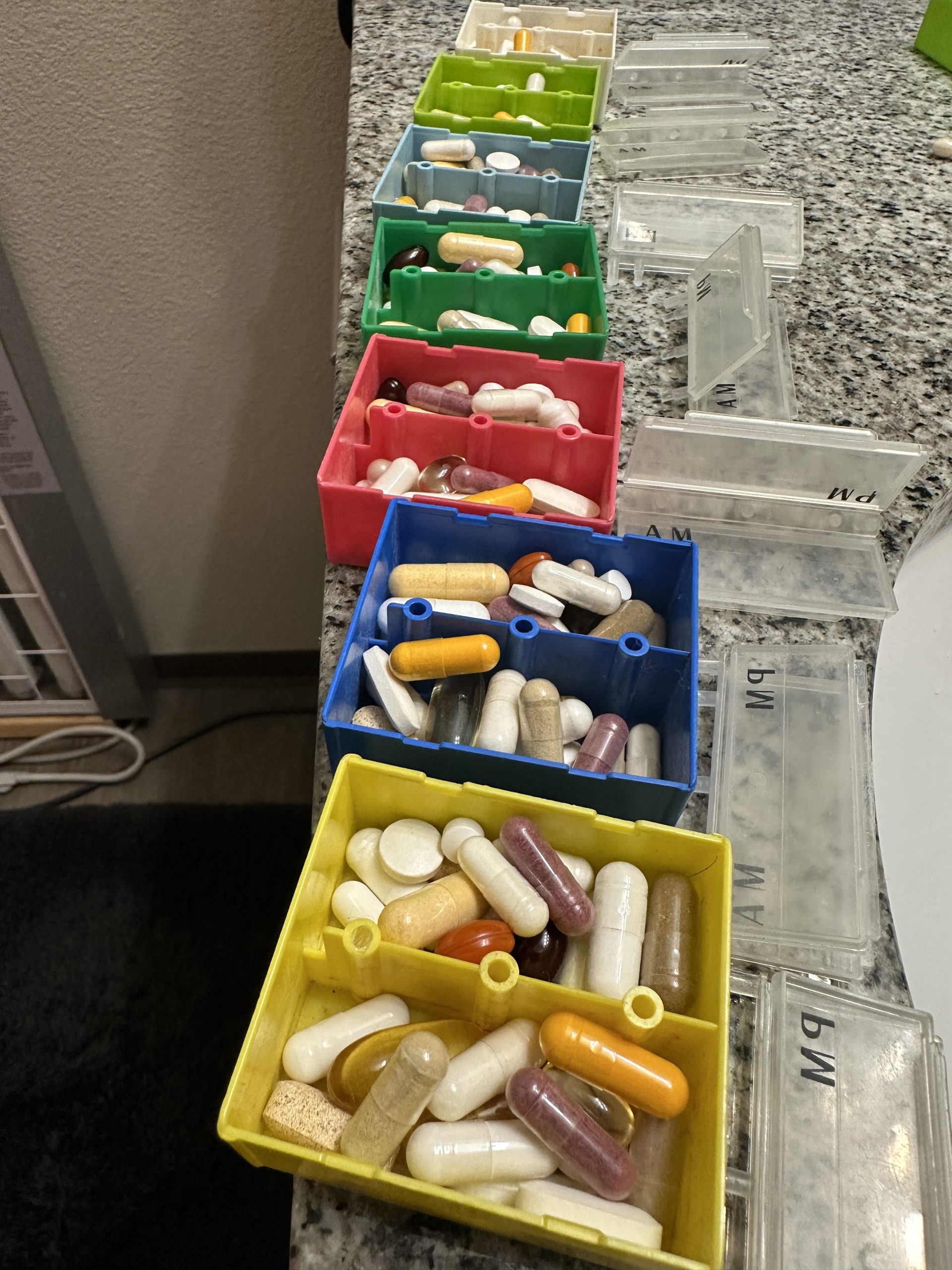 Assorted pill organizers filled with various capsules and tablets on a countertop.