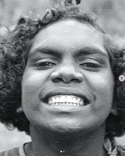 Young person with curly hair smiling broadly, showcasing bright white teeth against a plain background.