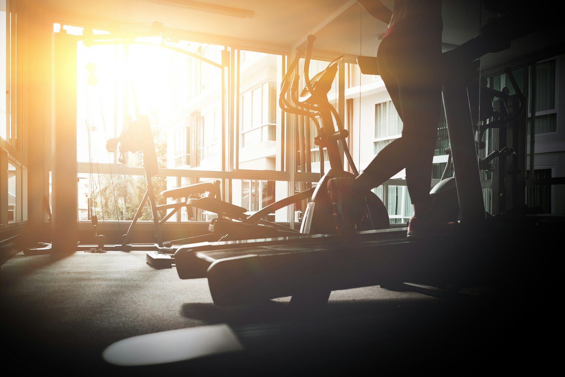Person using an elliptical machine in a brightly lit gym with exercise equipment nearby.