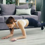 Woman in a plank position on a floor, exercising in a cozy living room with a sofa and plants.